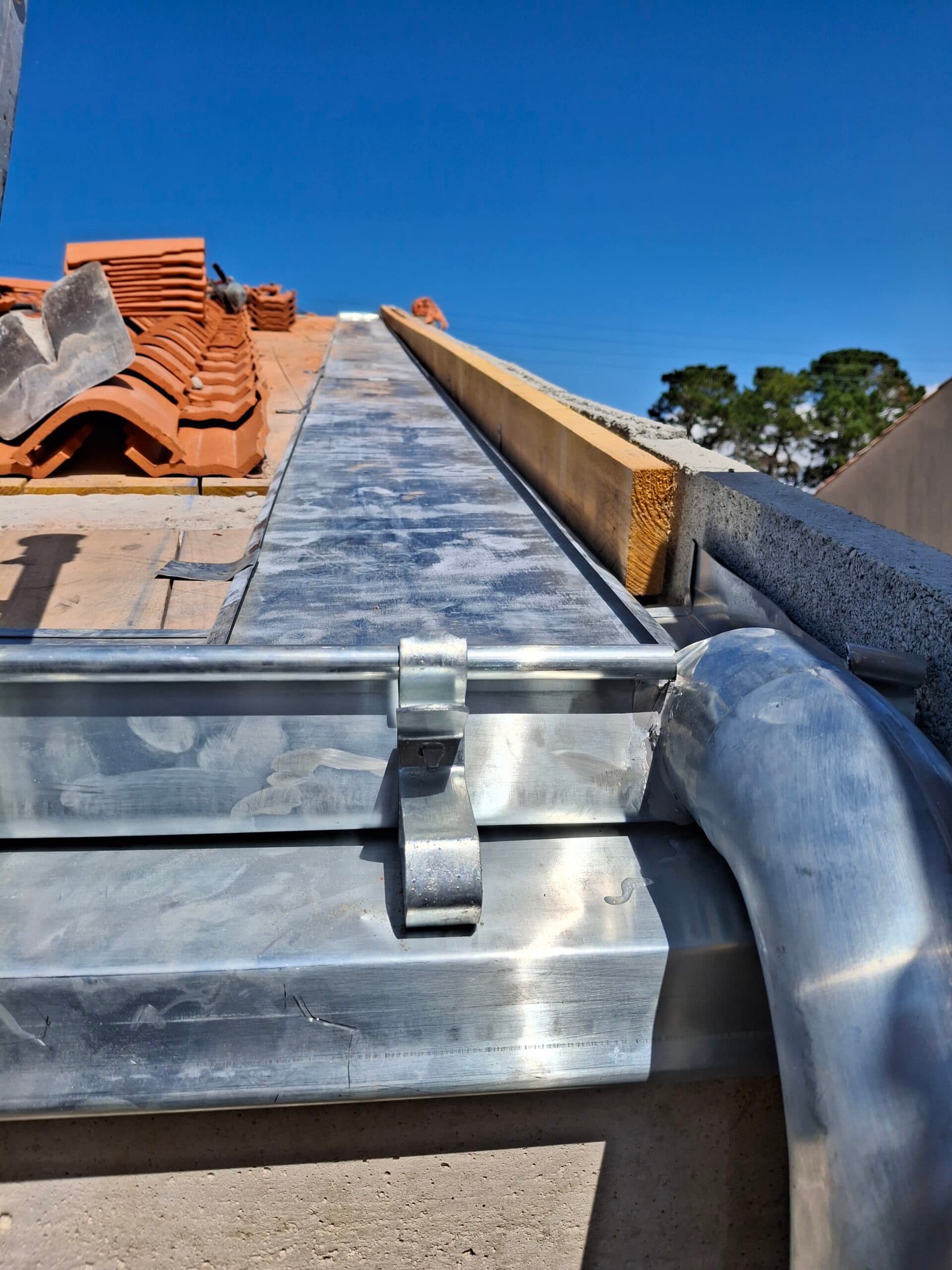 Chéneau en zinc installé sur une toiture en tuiles sous un ciel bleu dégagé.