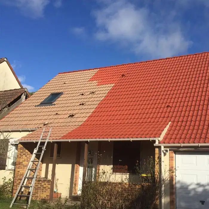 Toiture de maison partiellement rénovée montrant le contraste entre les tuiles anciennes et rouges.