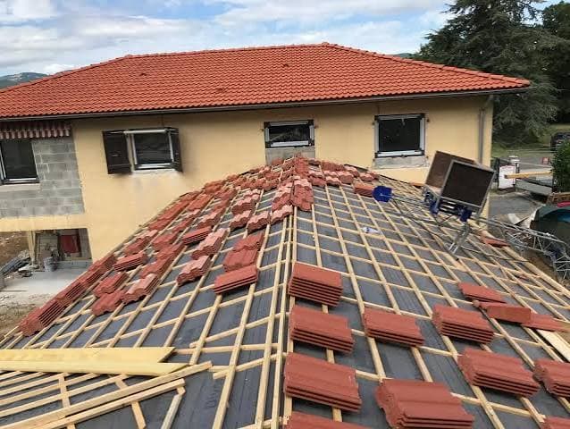 Installation de tuiles rouges en terre cuite sur la charpente en bois d'une maison.