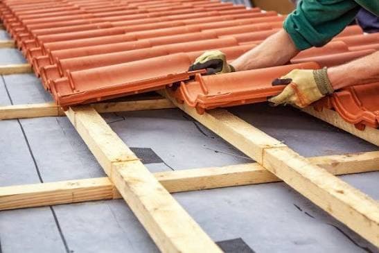 Couvreur posant des tuiles en terre cuite sur les liteaux en bois d'un toit.