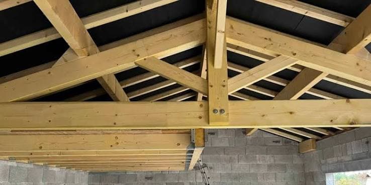 Charpente en bois apparente d'une maison en construction avec des murs en parpaings gris.