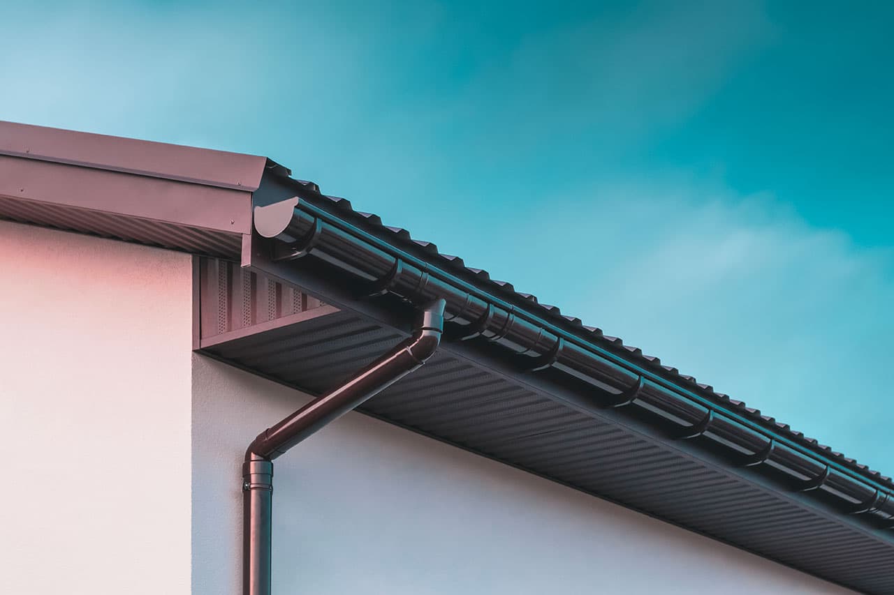 Gouttière noire et tuyau de descente fixés à une maison sous un ciel bleu.
