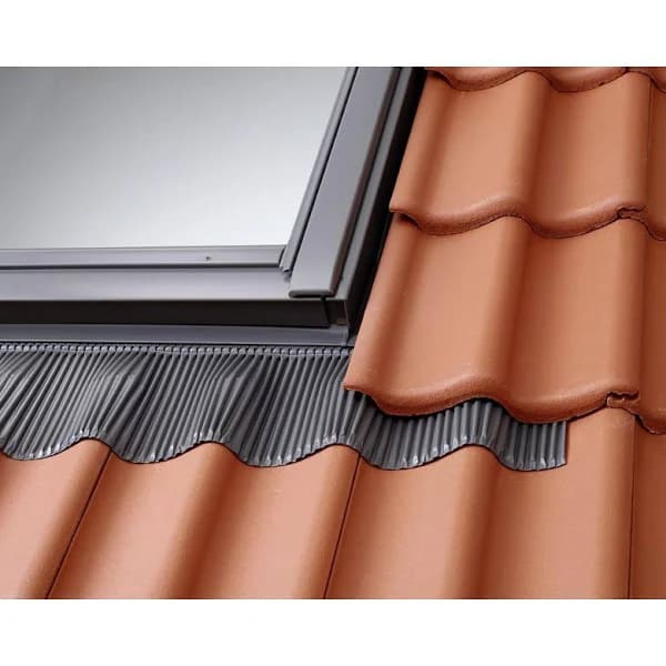 Fenêtre de toit installée sur des tuiles rouges avec un raccord d'étanchéité gris plissé.